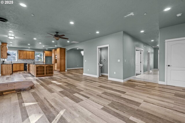 unfurnished living room featuring ceiling fan, a textured ceiling, and light wood-type flooring
