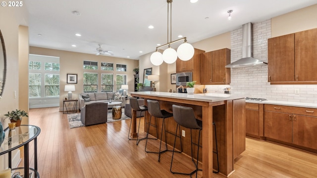kitchen with stainless steel microwave, tasteful backsplash, wall chimney exhaust hood, and light wood-type flooring