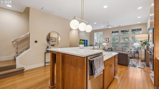 kitchen with visible vents, brown cabinets, open floor plan, light wood-style floors, and an island with sink