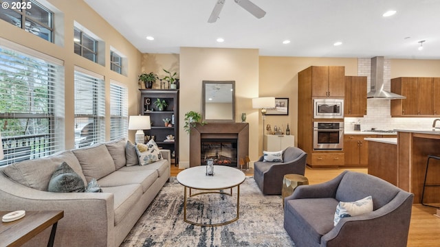 living room with recessed lighting, a ceiling fan, light wood finished floors, and a glass covered fireplace