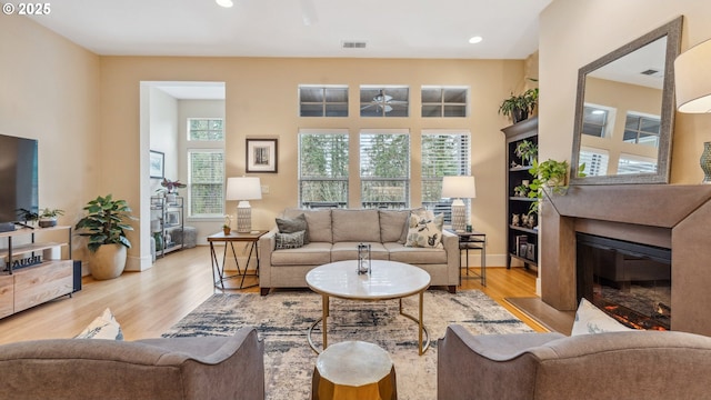 living room with ceiling fan, visible vents, wood finished floors, baseboards, and a glass covered fireplace