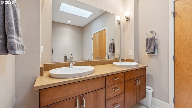 bathroom featuring baseboards, double vanity, a skylight, and a sink