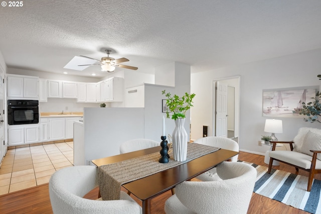 dining area featuring light wood finished floors, a skylight, recessed lighting, ceiling fan, and a textured ceiling