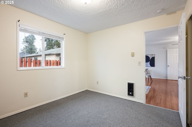 unfurnished room with heating unit, carpet, baseboards, and a textured ceiling