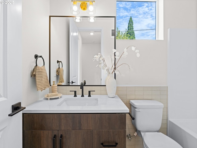 bathroom featuring tile walls, toilet, wainscoting, vanity, and a tub