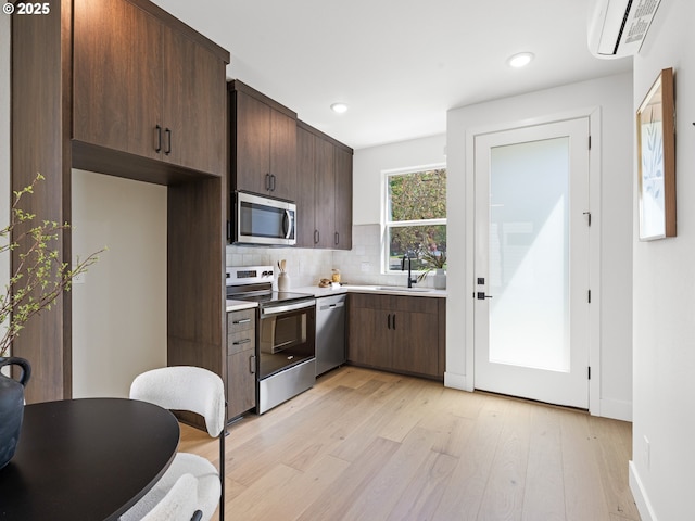 kitchen with appliances with stainless steel finishes, a wall unit AC, dark brown cabinetry, light countertops, and light wood-type flooring