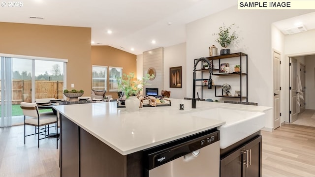 kitchen with visible vents, stainless steel dishwasher, a large fireplace, vaulted ceiling, and light wood-type flooring