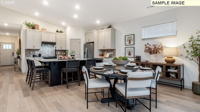 kitchen featuring stainless steel fridge, a center island with sink, a breakfast bar area, and light countertops