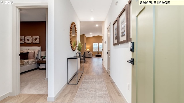 hall with light wood-style floors, baseboards, and vaulted ceiling