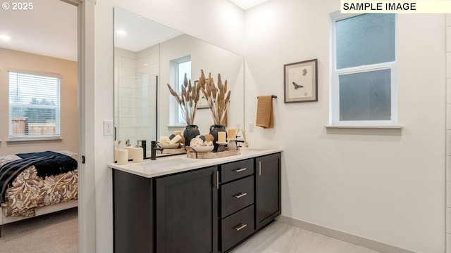 ensuite bathroom with double vanity, a sink, a tile shower, ensuite bath, and baseboards