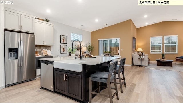 kitchen with stainless steel appliances, a sink, vaulted ceiling, light countertops, and an island with sink