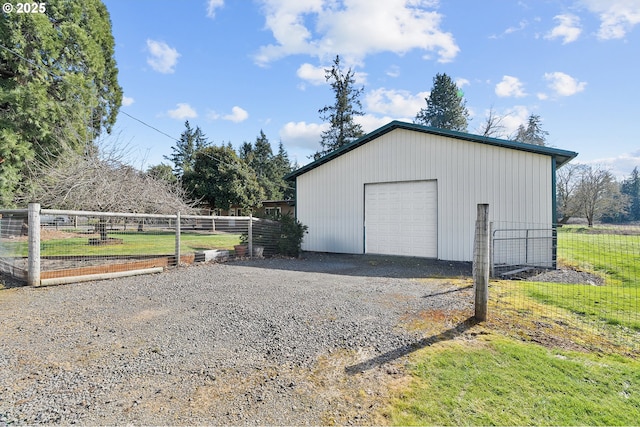 detached garage with driveway, a vegetable garden, and fence