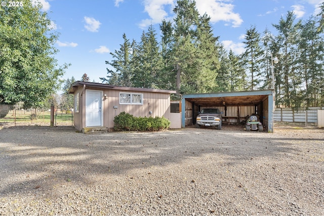 view of outbuilding with a detached carport, gravel driveway, an outdoor structure, and fence