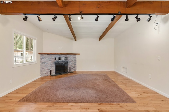 unfurnished living room featuring light wood-type flooring, beamed ceiling, baseboards, and a brick fireplace