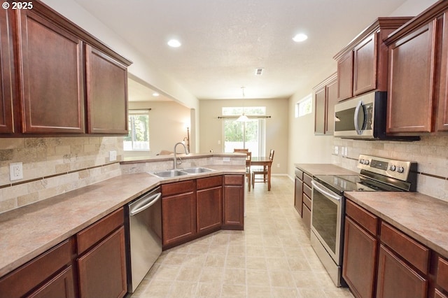 kitchen featuring stainless steel appliances, a sink, decorative backsplash, recessed lighting, and a peninsula