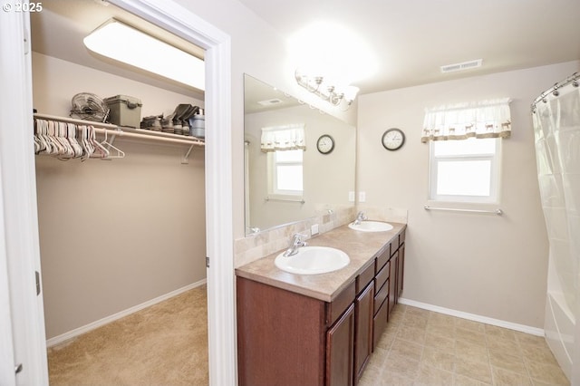 full bath featuring a walk in closet, baseboards, and double vanity