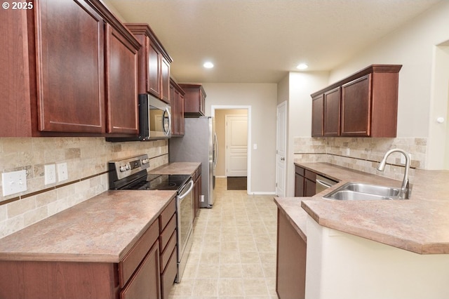 kitchen featuring stainless steel appliances, a sink, a peninsula, recessed lighting, and backsplash