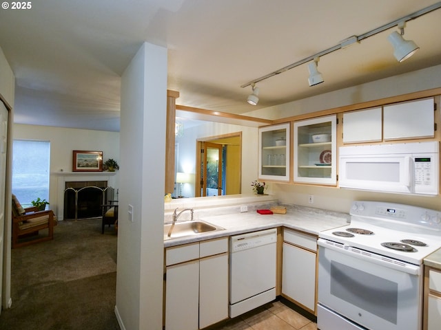 kitchen featuring glass insert cabinets, light countertops, a tile fireplace, white appliances, and a sink