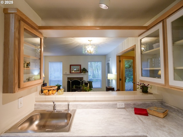 kitchen featuring an inviting chandelier, glass insert cabinets, light countertops, and a sink