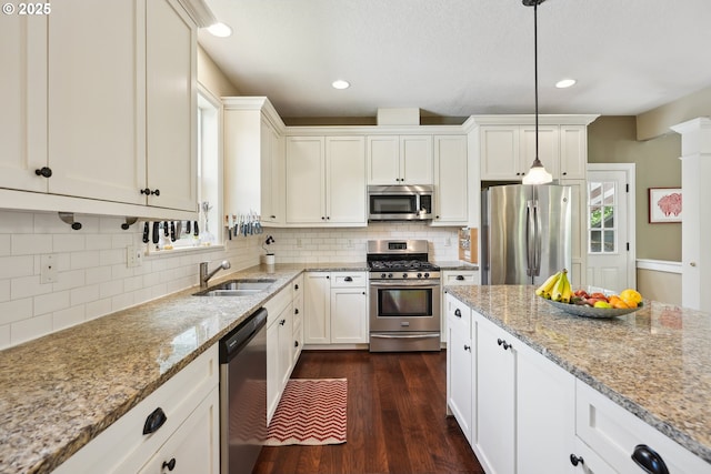 kitchen featuring appliances with stainless steel finishes, a sink, backsplash, dark wood-type flooring, and light stone counters