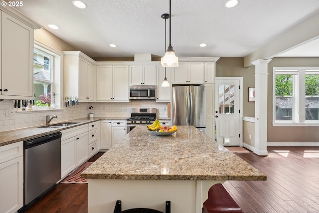 kitchen with appliances with stainless steel finishes, a sink, backsplash, light stone counters, and a kitchen island