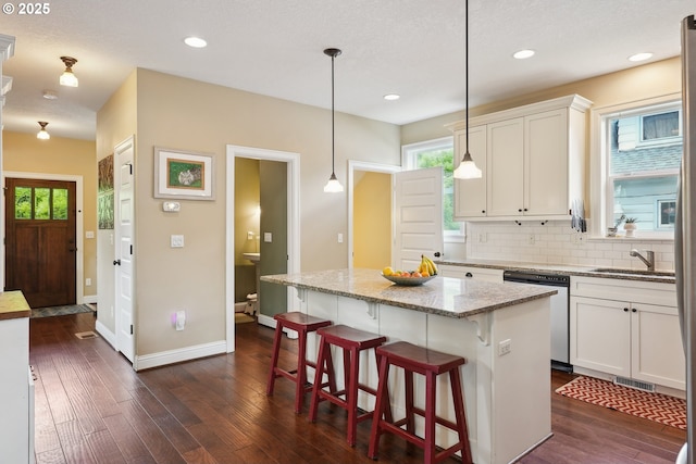 kitchen with dishwasher, a sink, dark wood-style floors, tasteful backsplash, and white cabinets