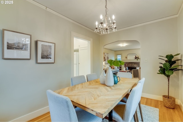 dining area featuring crown molding, a notable chandelier, light wood-style floors, and arched walkways