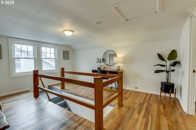 bedroom with baseboards, a textured ceiling, vaulted ceiling, and light wood finished floors