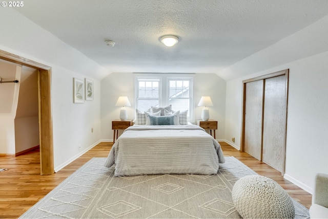 bedroom featuring a closet, a textured ceiling, lofted ceiling, and light wood-style floors