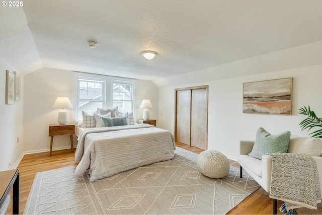 bedroom featuring baseboards, a textured ceiling, lofted ceiling, and light wood-style floors