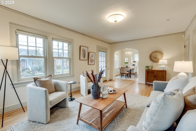 living area featuring an inviting chandelier, baseboards, arched walkways, and light wood-type flooring