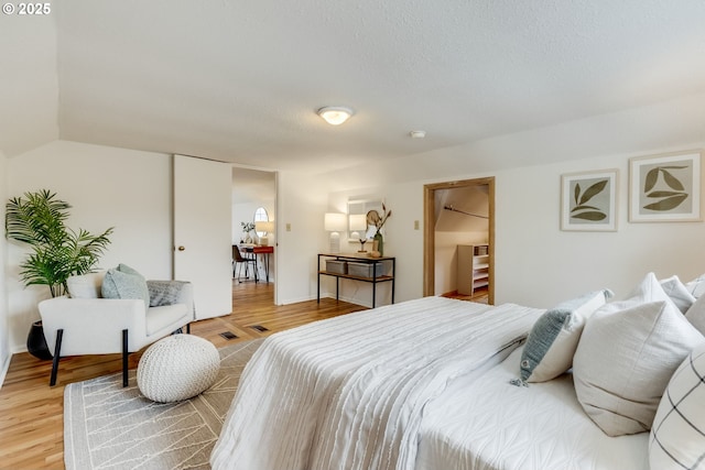 bedroom featuring baseboards, a textured ceiling, lofted ceiling, and light wood-style floors