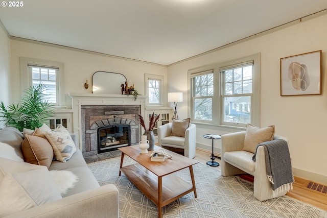 living room with visible vents, baseboards, a glass covered fireplace, and light wood finished floors