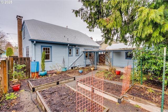 rear view of property featuring a chimney, fence, and a garden