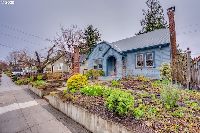 view of front of house with a garden, a chimney, and fence