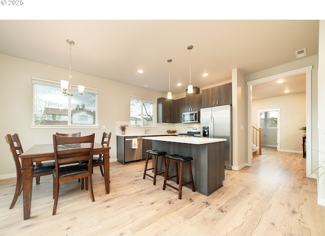 kitchen featuring hanging light fixtures, dark brown cabinets, a center island, and appliances with stainless steel finishes