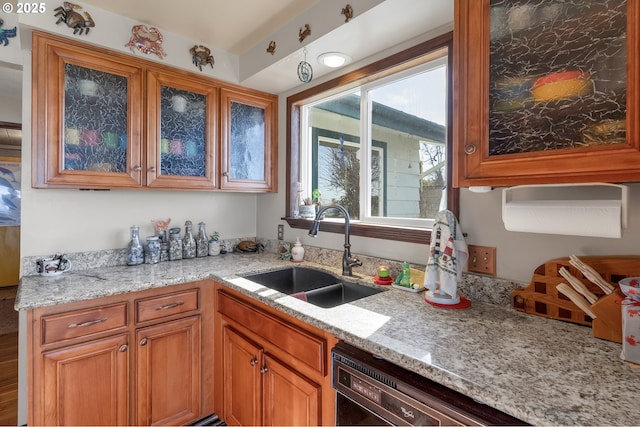 kitchen with glass insert cabinets, dishwasher, a sink, brown cabinets, and light stone counters