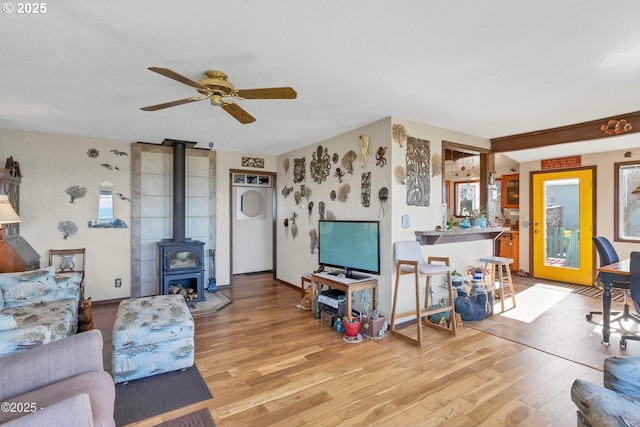 living room with light wood finished floors, ceiling fan, and a wood stove