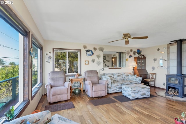 living room featuring light wood finished floors, a wood stove, and a ceiling fan
