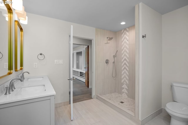 full bath featuring toilet, baseboards, tiled shower, and a sink