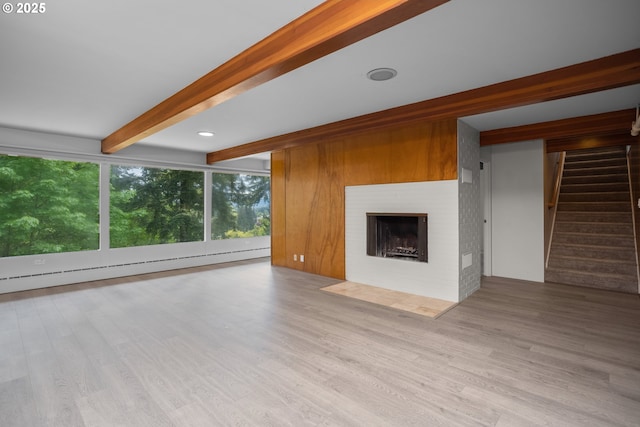 unfurnished living room with wood finished floors, a brick fireplace, stairway, baseboard heating, and beamed ceiling