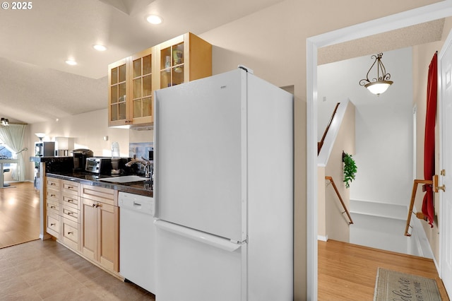kitchen featuring dark countertops, a sink, white appliances, recessed lighting, and glass insert cabinets