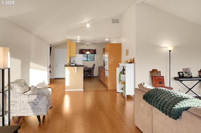 living room featuring light wood-style floors, baseboards, vaulted ceiling, and visible vents