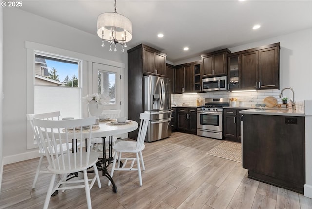 kitchen with light wood finished floors, backsplash, dark brown cabinetry, light countertops, and appliances with stainless steel finishes