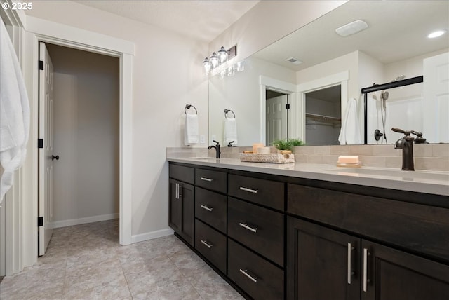 bathroom with double vanity, a stall shower, baseboards, and a sink