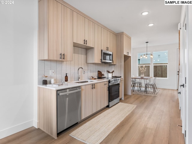 kitchen with tasteful backsplash, stainless steel appliances, light countertops, light wood-style floors, and a sink