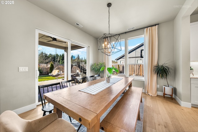 dining space with ceiling fan with notable chandelier, light hardwood / wood-style floors, and a wealth of natural light