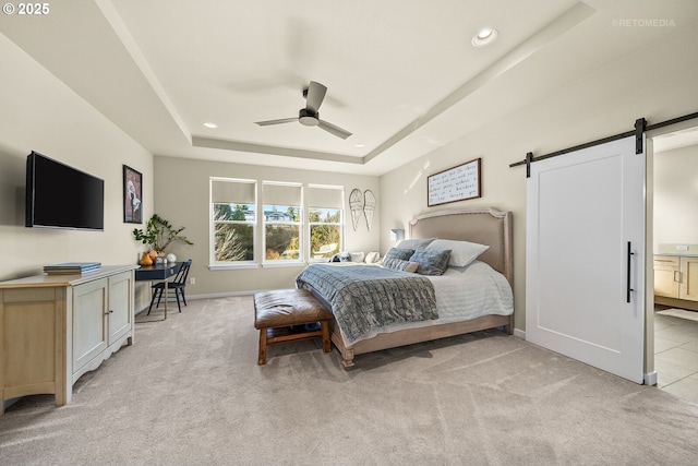 carpeted bedroom featuring ceiling fan, a barn door, a raised ceiling, and ensuite bath