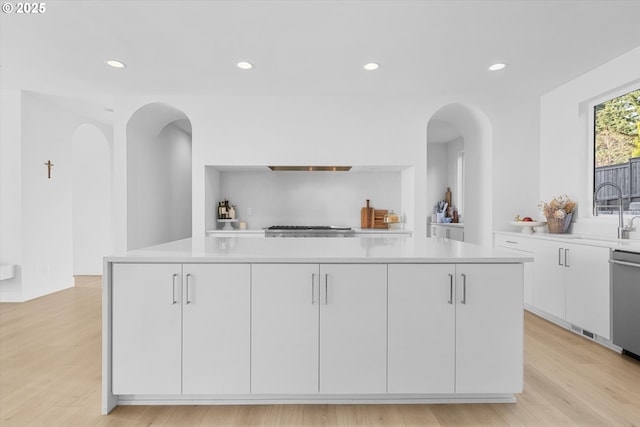 kitchen with a kitchen island, white cabinetry, sink, stainless steel appliances, and light hardwood / wood-style flooring