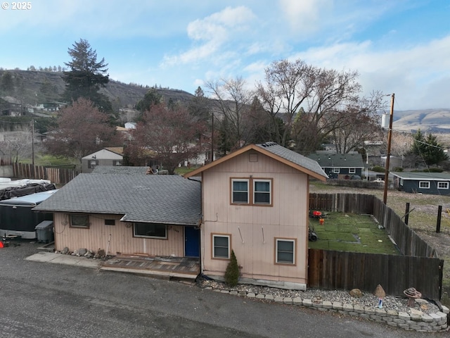 exterior space featuring a front lawn, roof with shingles, a fenced backyard, and a mountain view